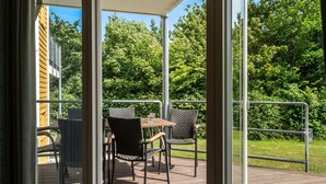 An outdoor patio with wicker furniture and a table, overlooking a lush green landscape. - Gudhjem Søpark Lejl. 23 (Gudhjem)