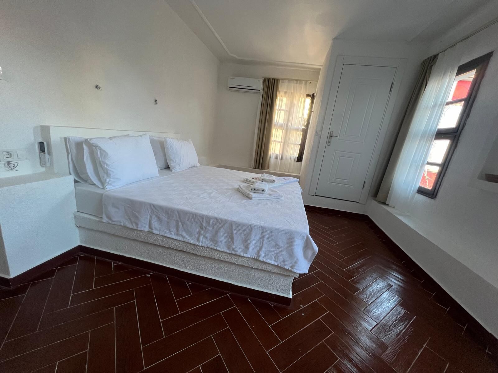 A hotel room with a large bed, a bedside table, a wardrobe, and a window with curtains.