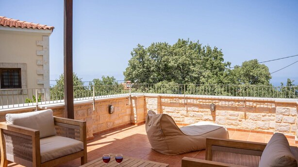 A terrace with wicker furniture, a stone wall, and a view of trees.