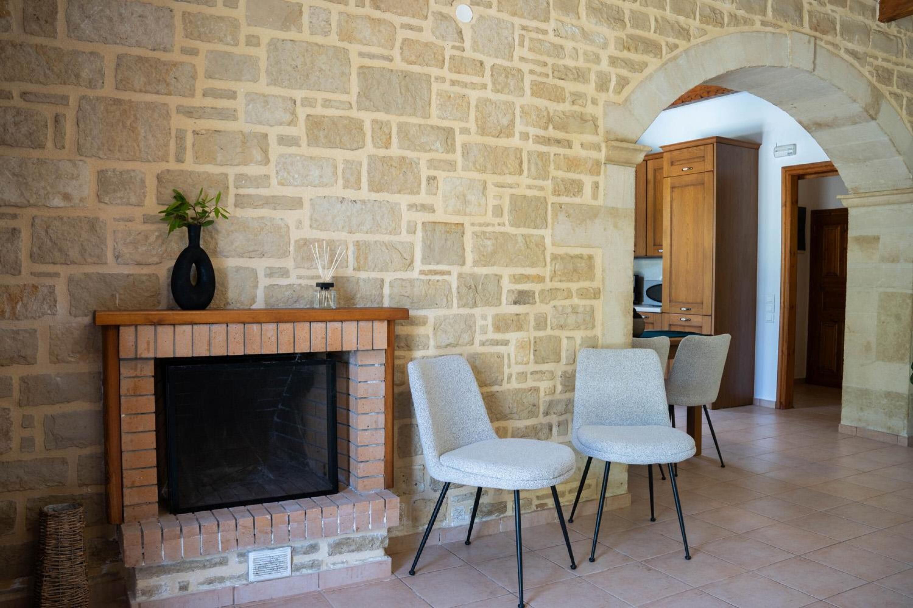 A stone-walled room with a fireplace, two chairs, and a wooden cabinet.