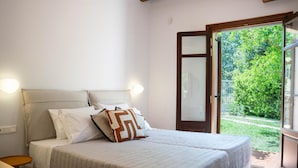 A double bed with a beige quilt, white pillows, and a geometric patterned pillow. There is a small wooden table beside the bed.
