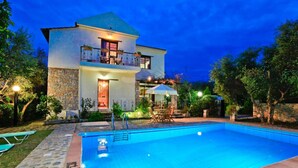 Ein zweistöckiges Haus mit Swimmingpool, Steinhausfassade und Sitzgelegenheit im Freien.