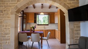 Una cocina con paredes de piedra, armarios de madera, una mesa de comedor con sillas y un televisor montado en la pared.