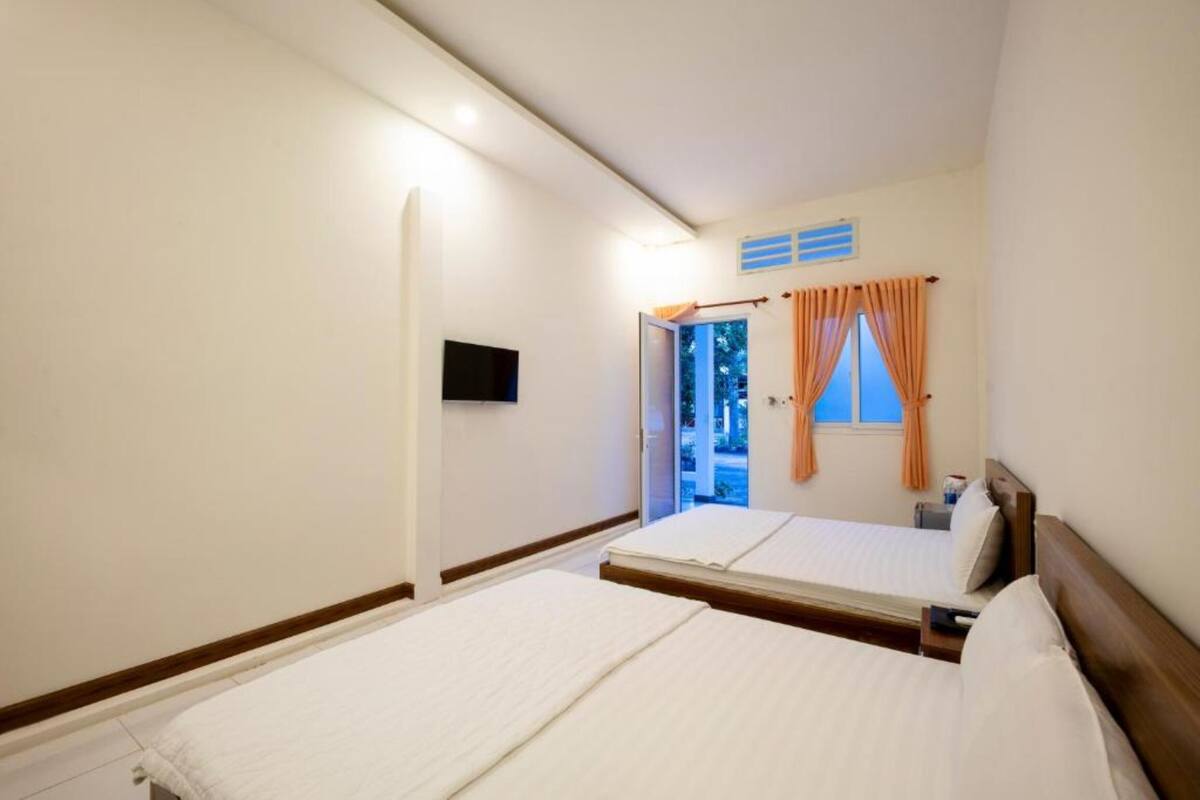 A hotel room with two beds, a television, and a window with curtains.