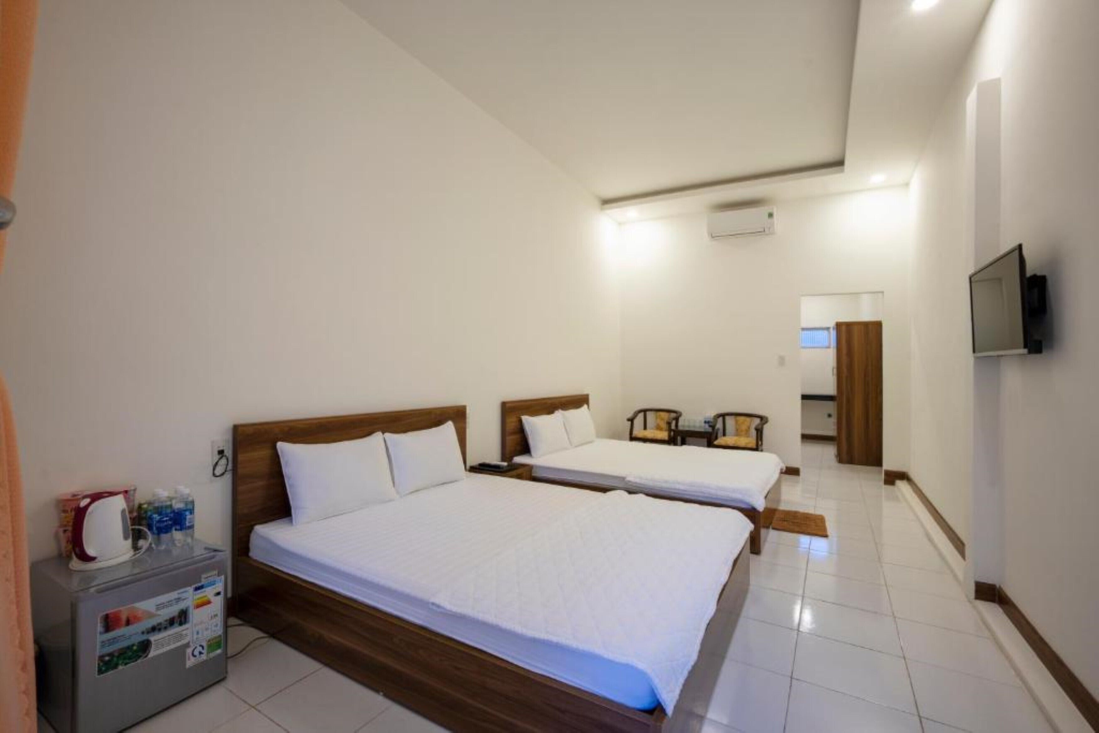 A hotel room with two beds, a small table with a kettle, and a TV on the wall.