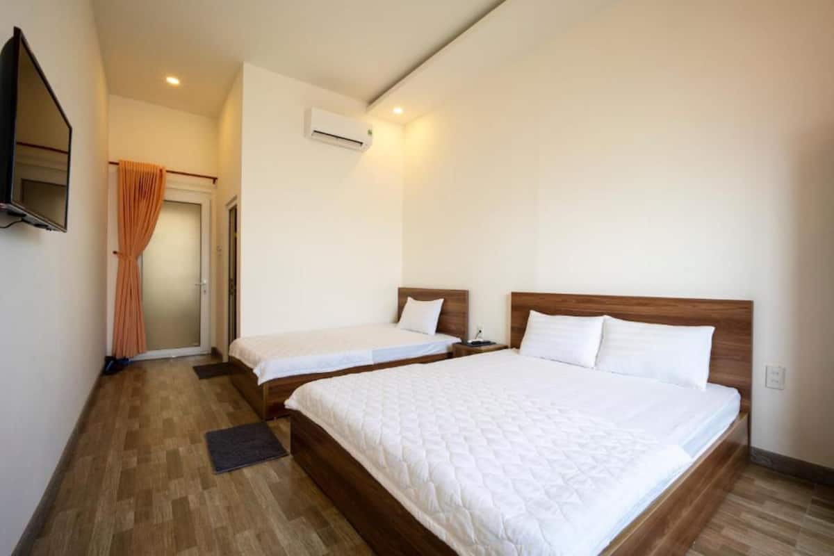 A hotel room with two beds, a television, an air conditioning unit, and a wooden floor.