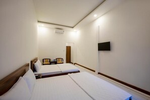 A hotel room with two single beds, a wooden headboard, a flat-screen TV mounted on the wall, a small table with a chair, and a door leading to another room. - Phu Quoc Hotel (Phu Quoc)