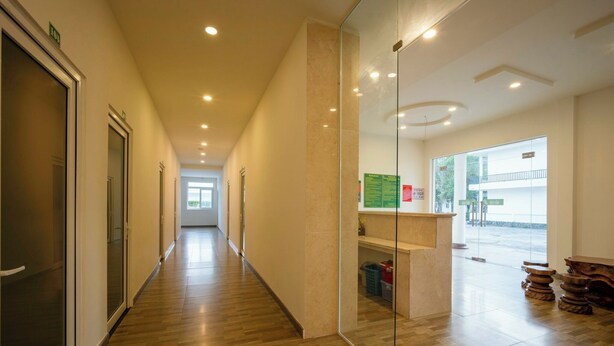 Un corridoio con pavimento in legno, pareti divisorie in vetro e una reception che si affaccia all'esterno.