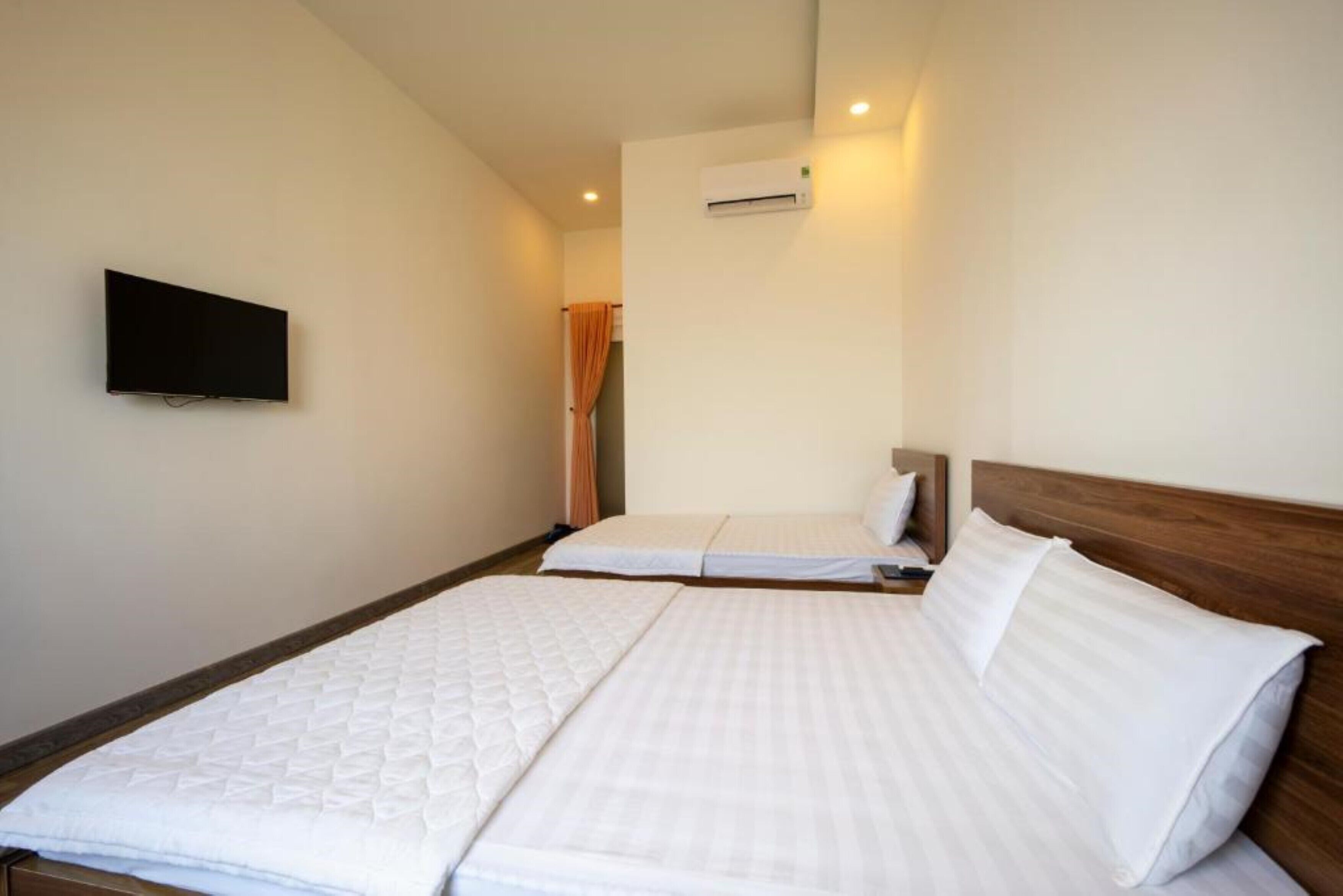 A hotel room with two beds, a flat-screen TV mounted on the wall, and an air conditioning unit.