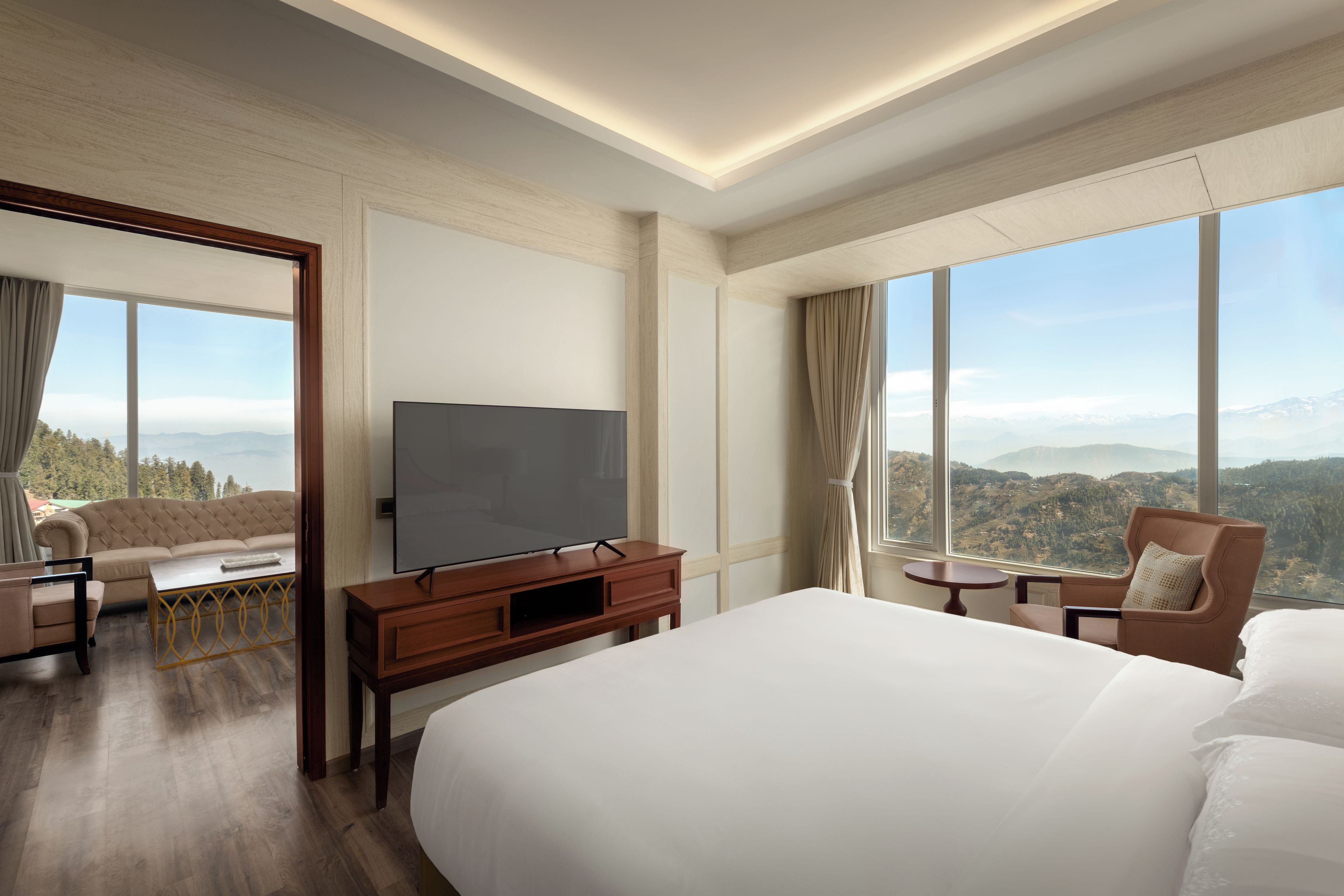 Habitación de hotel con una cama grande, televisor, sofá, una mesita y vistas a la montaña.