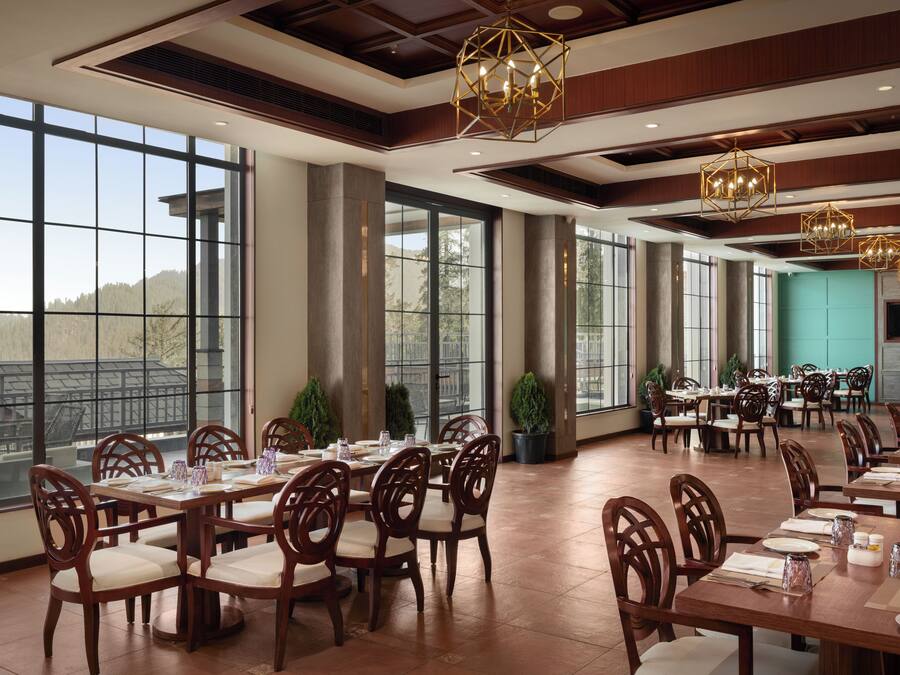 Un comedor amplio con ventanas grandes, mesas y sillas de madera, y vistas al exterior.