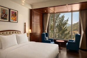 A hotel room with a large bed, two armchairs, a small table, and a view of a forest through a large window. - Greenberry Resort Narkanda, a member of Radisson Individuals Premier (Kumharsain)