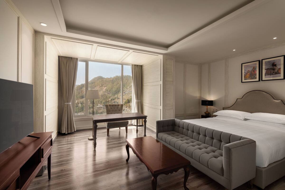 Une chambre d’hôtel avec un grand lit, un canapé, un bureau et une vue sur un paysage montagneux.
