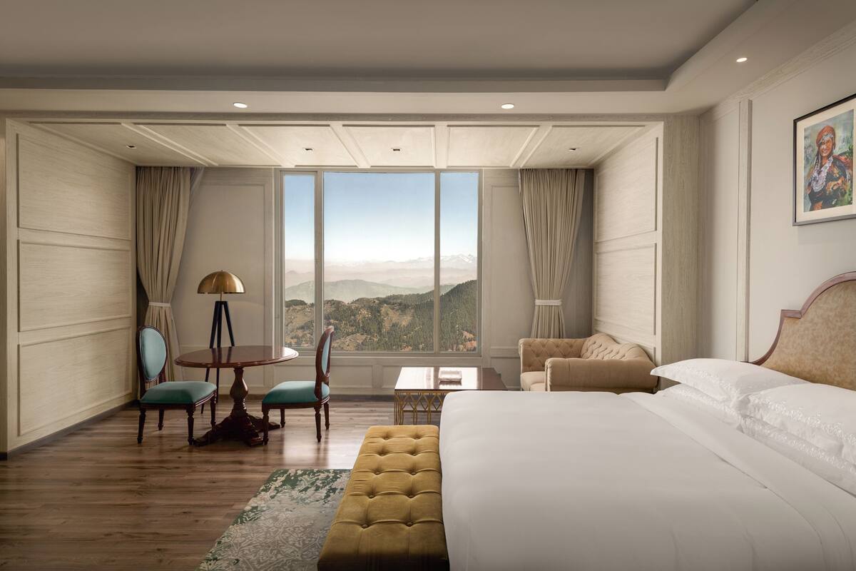 Une chambre d’hôtel avec un grand lit, un coin salon avec une table et des chaises, et une vue sur les montagnes.