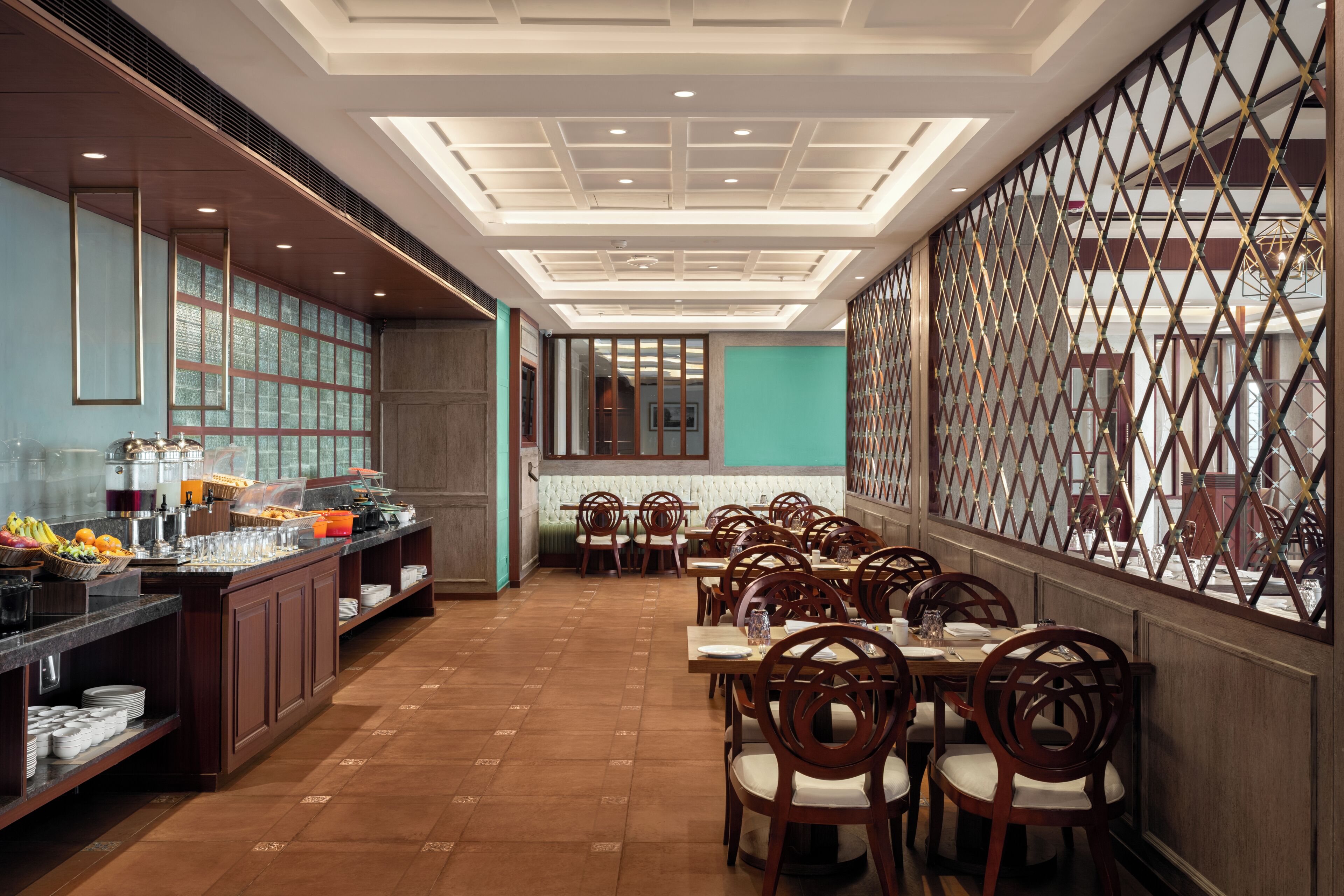 A hotel dining area with a buffet, wooden chairs, and a patterned wall.