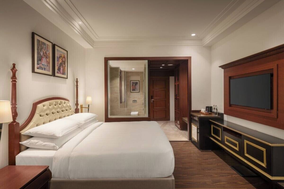 Une chambre d’hôtel avec un grand lit, une télévision, une armoire en bois et des œuvres d’art encadrées accrochées au mur.