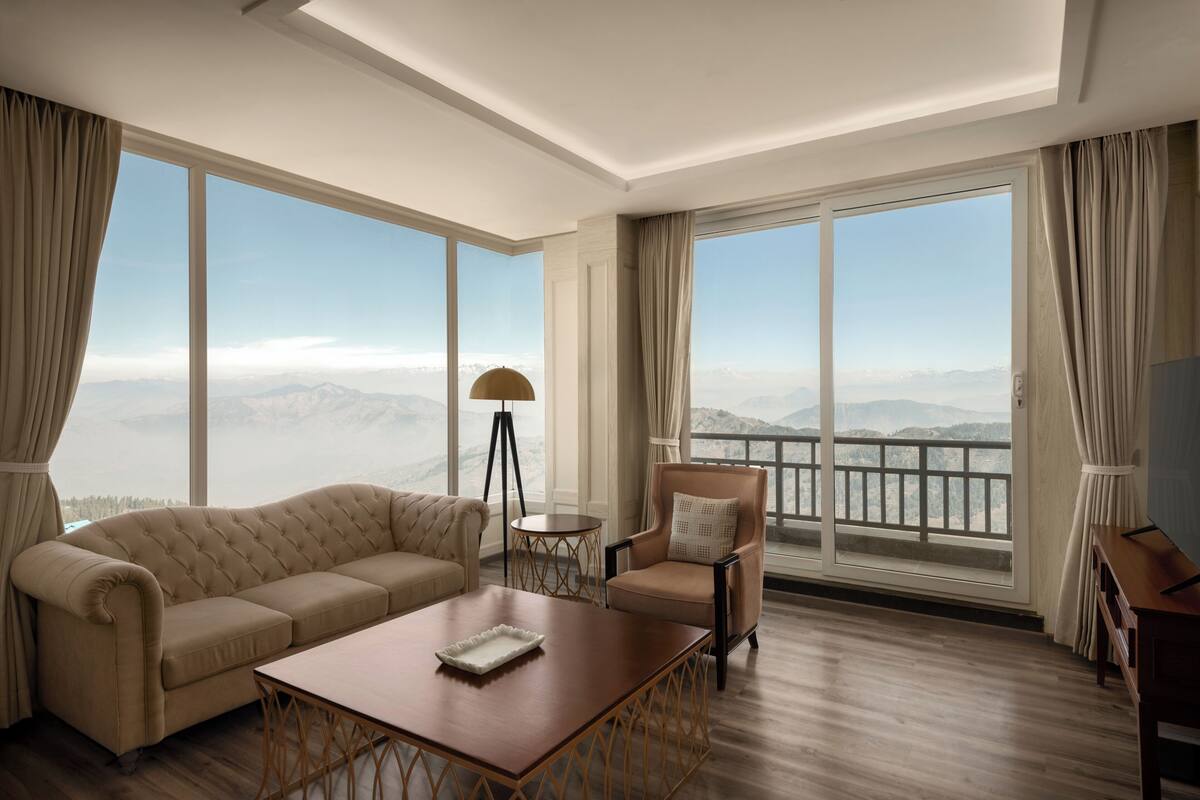 Une chambre d’hôtel moderne dotée d’une grande fenêtre, d’un canapé, d’un fauteuil, d’une table basse et d’une lampe.