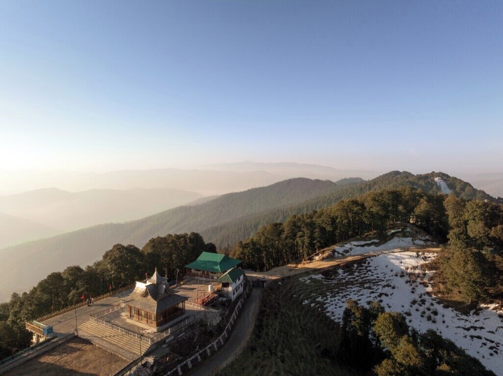 Un chalet de montagne doté d’un toit végétalisé, entouré de collines boisées et surplombant un ciel dégagé.