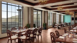 Un'ampia sala da pranzo con grandi finestre, tavoli e sedie in legno e vista sull'esterno.