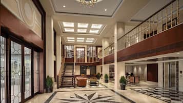 A spacious lobby with a grand chandelier, a checkered floor pattern, and a staircase leading to an upper level.