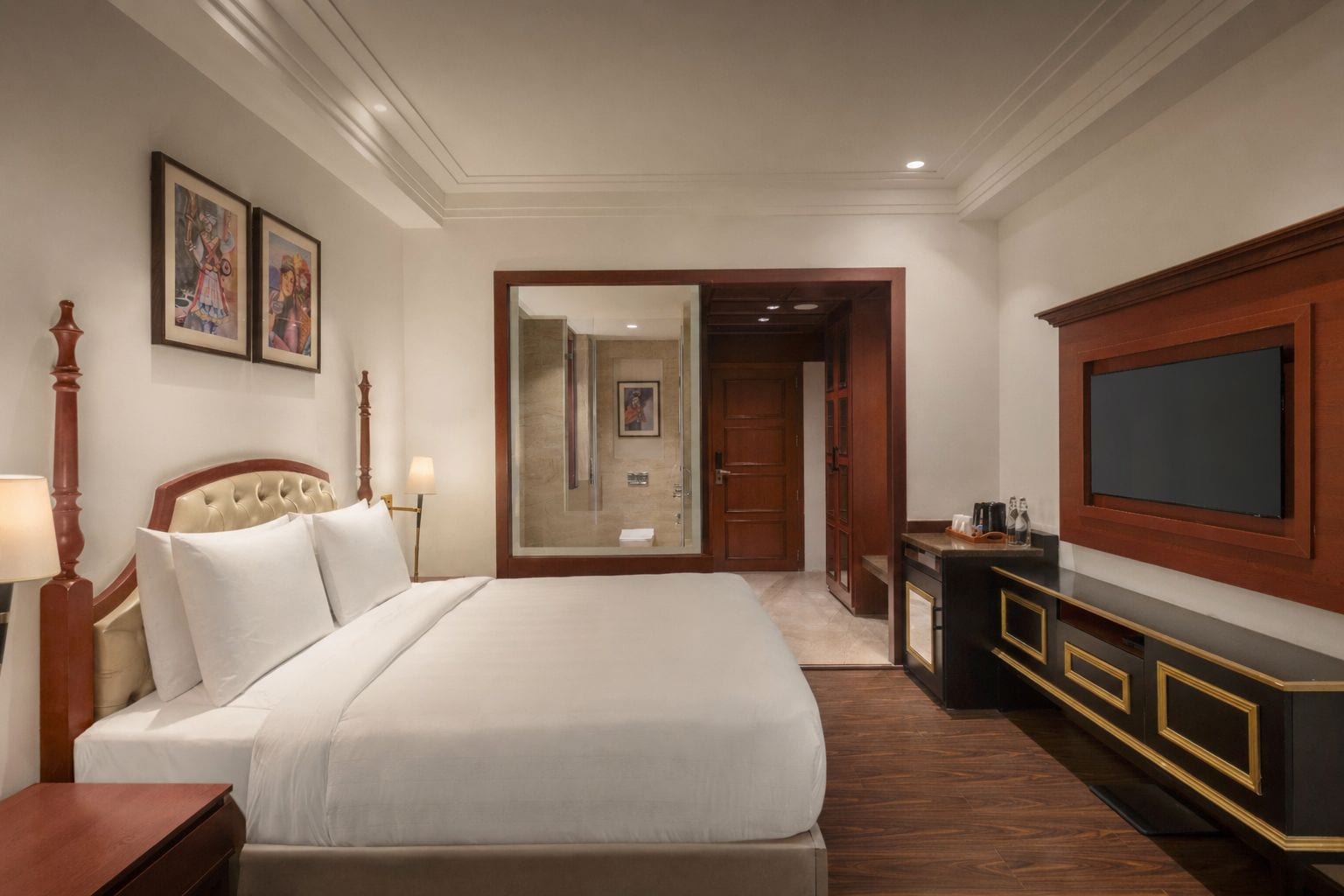 A hotel room with a large bed, a TV, a desk, and a mirror.