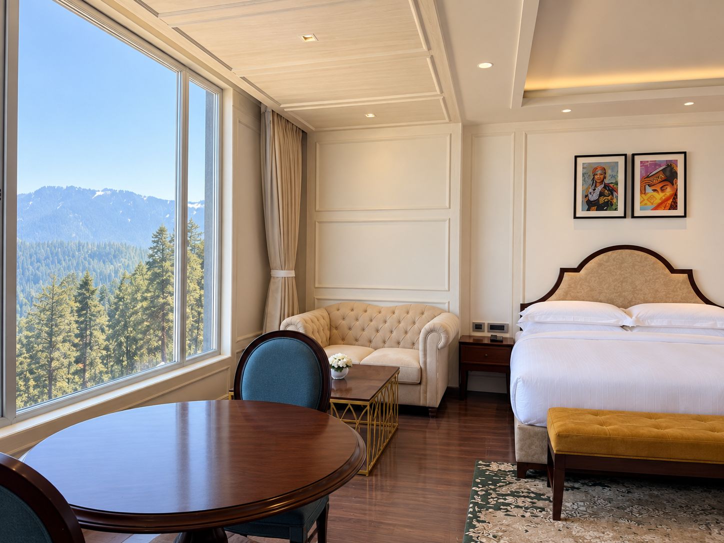 A hotel room with a bed, a chair, a table, and a view of a forest through a large window.
