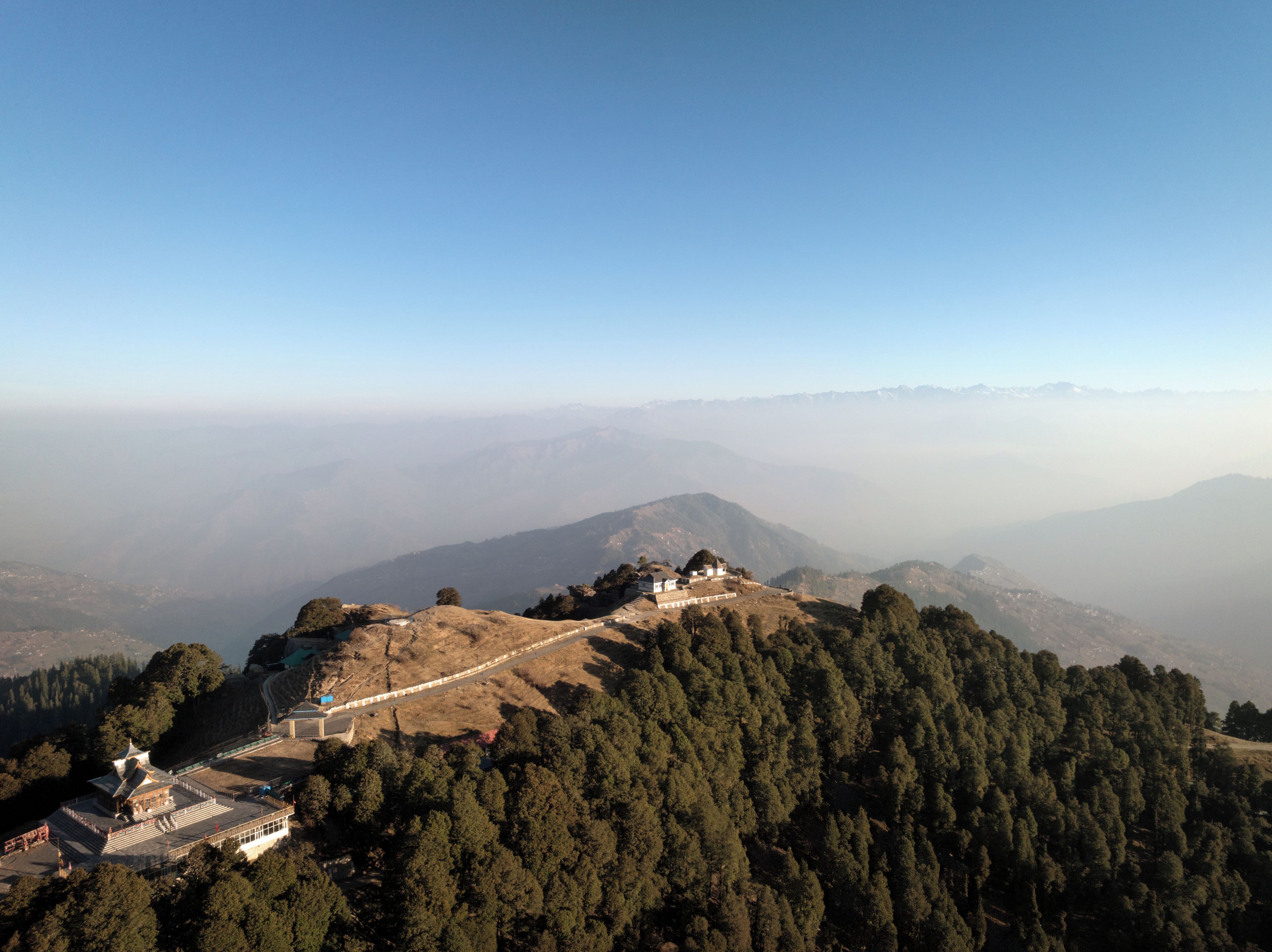 Un paisaje montañoso con un edificio en la cima de una colina, rodeado de un bosque denso.