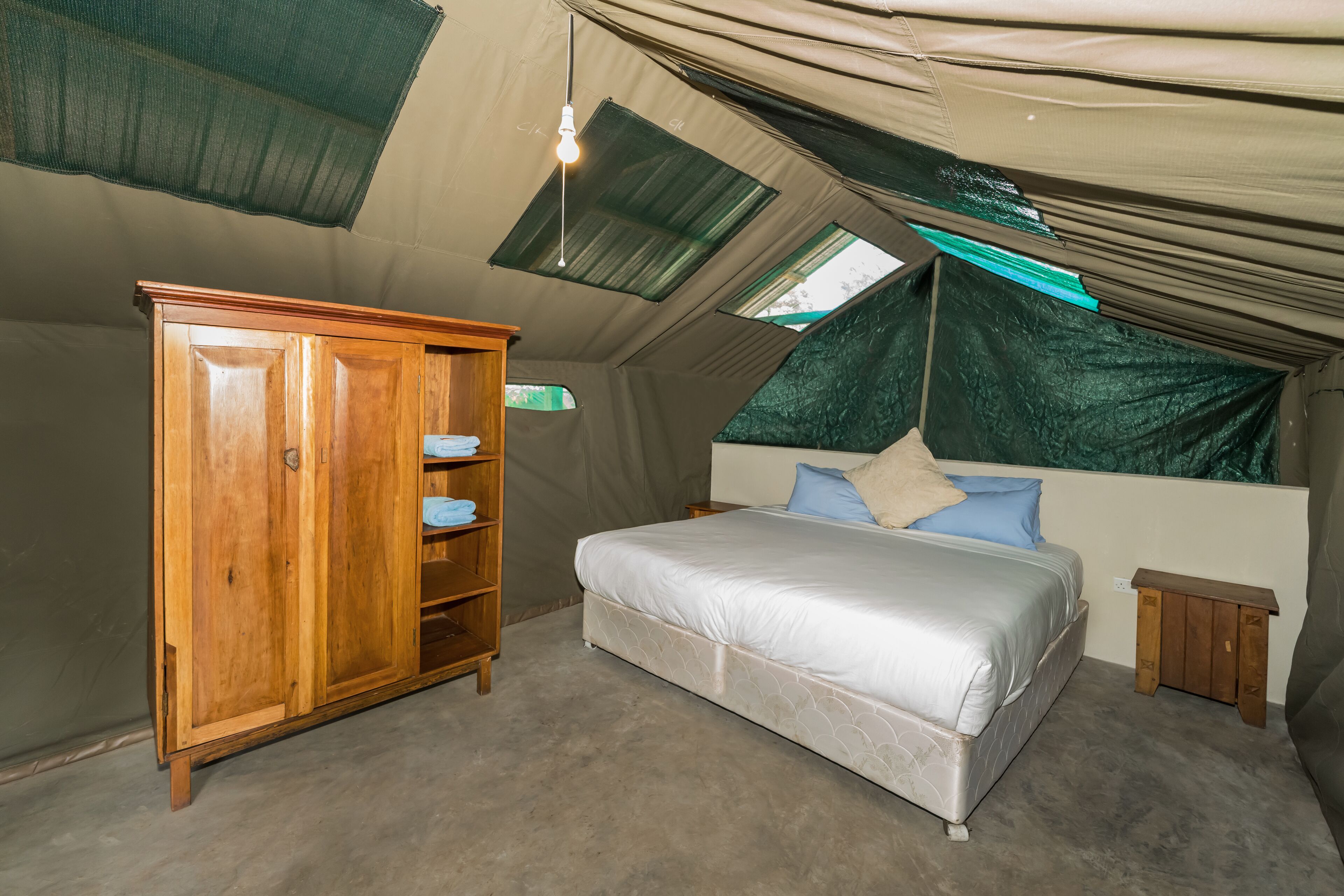 Ein Zeltraum mit Bett, Holzschrank und Dachfenster.