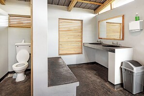 Un baño con inodoro, lavamanos, espejo y persianas.