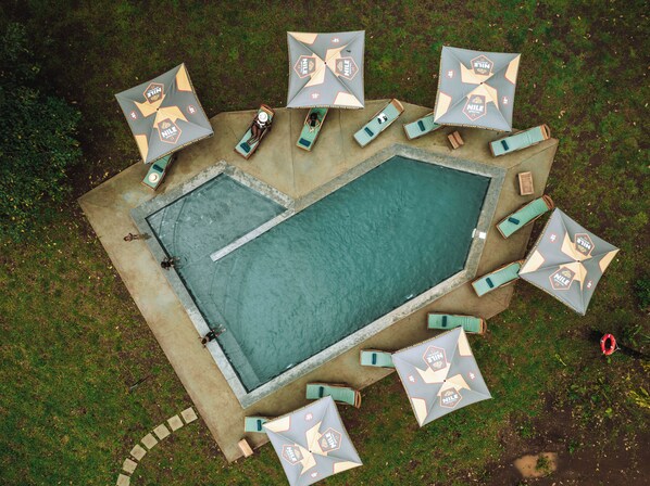 Vista aérea de un área de piscina con múltiples sillas de descanso y sombrillas, rodeada por una terraza de concreto.