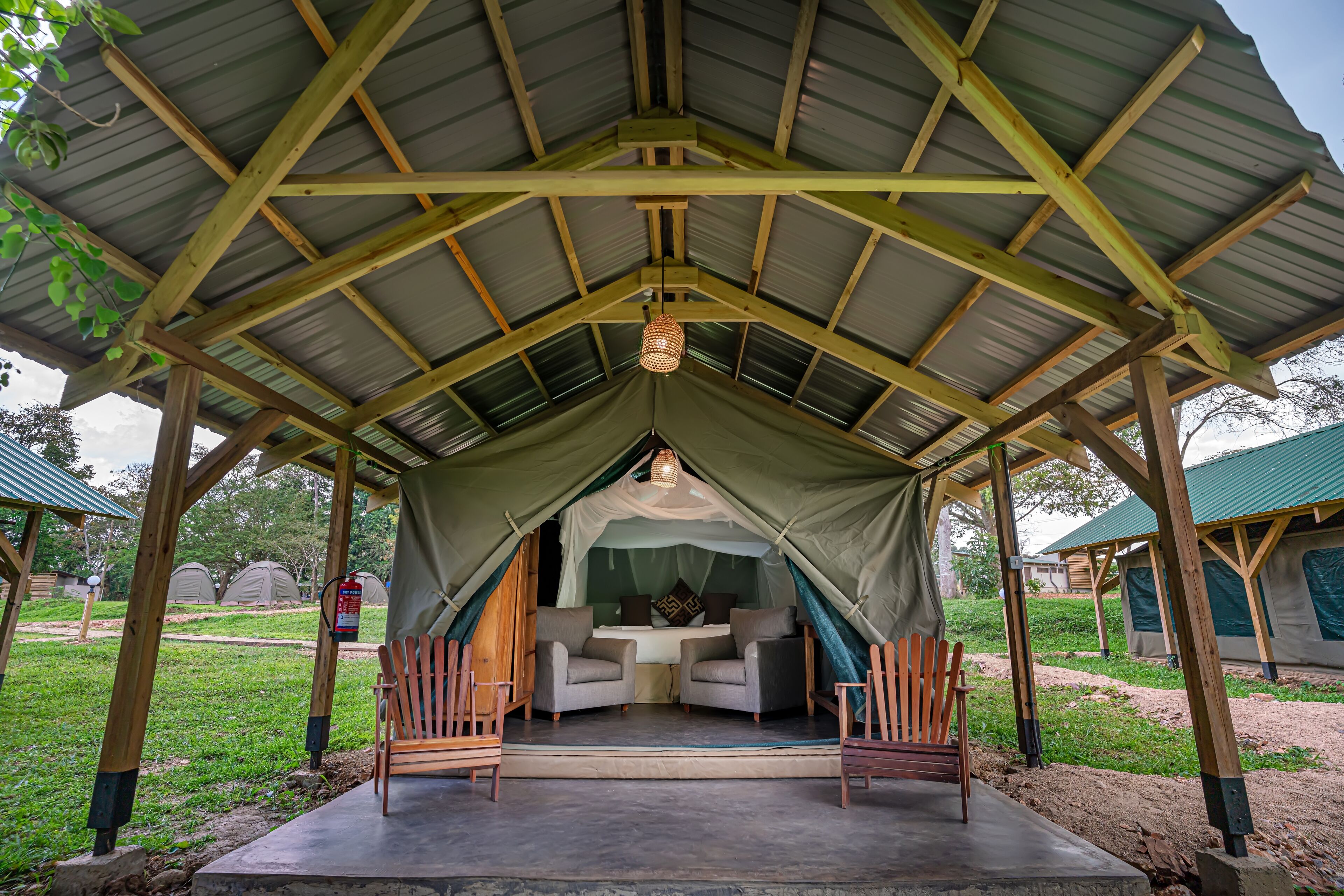 A tented accommodation with a central bed area, two chairs, and a hanging light fixture.