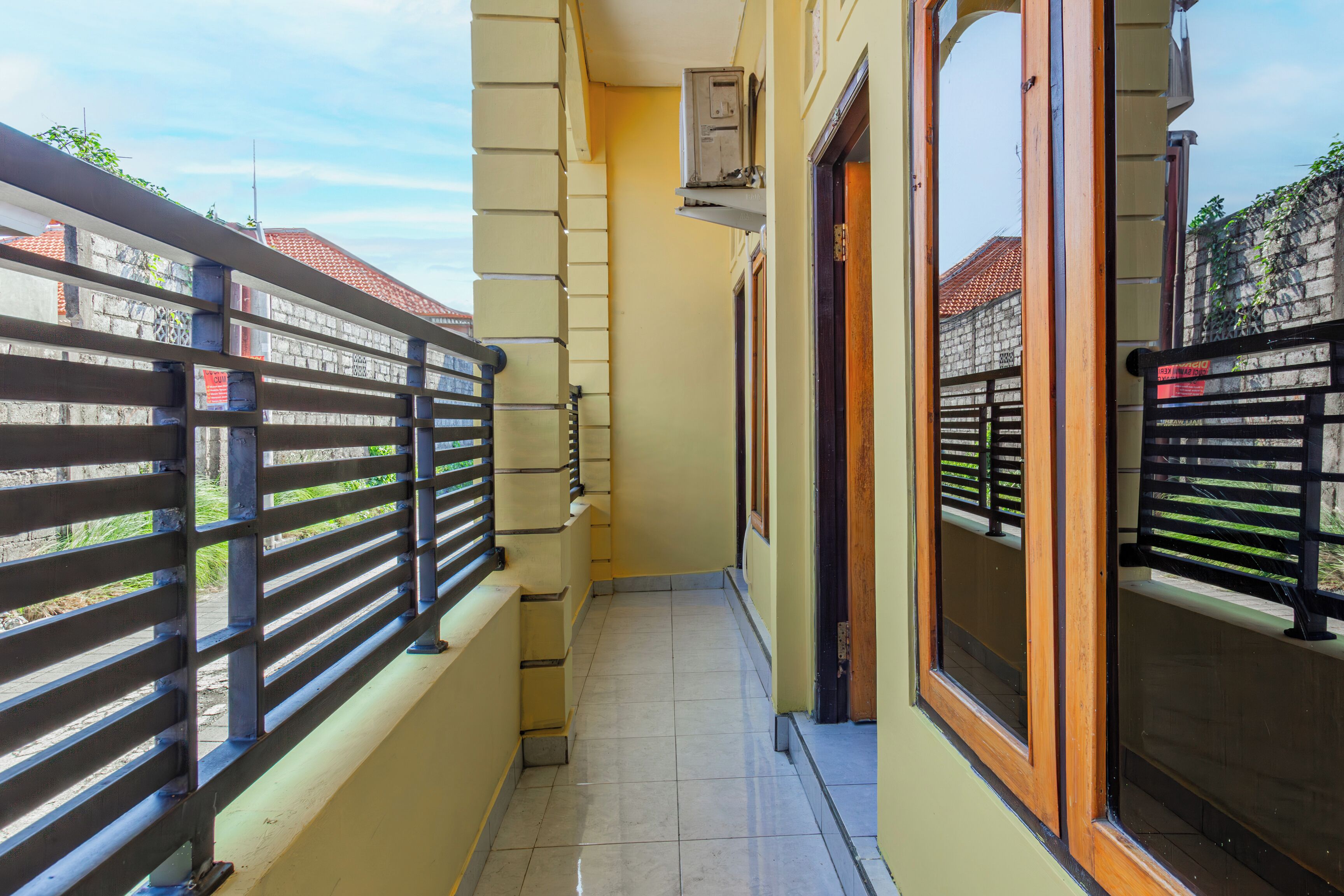 A narrow balcony with metal railings, a tiled floor, and a view of buildings in the background.