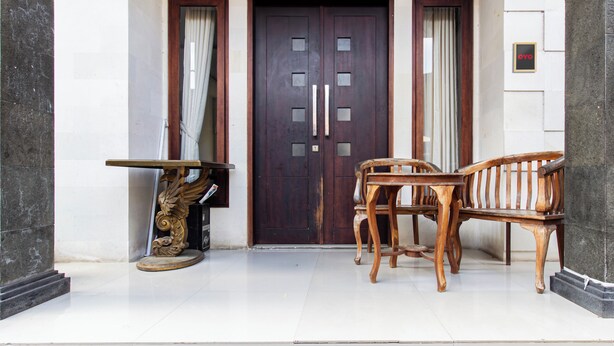 A dark wooden door with glass panels, flanked by curtains, and a small round table with a chair to the left. - OYO 94091 Sn Guest House (Denpasar)