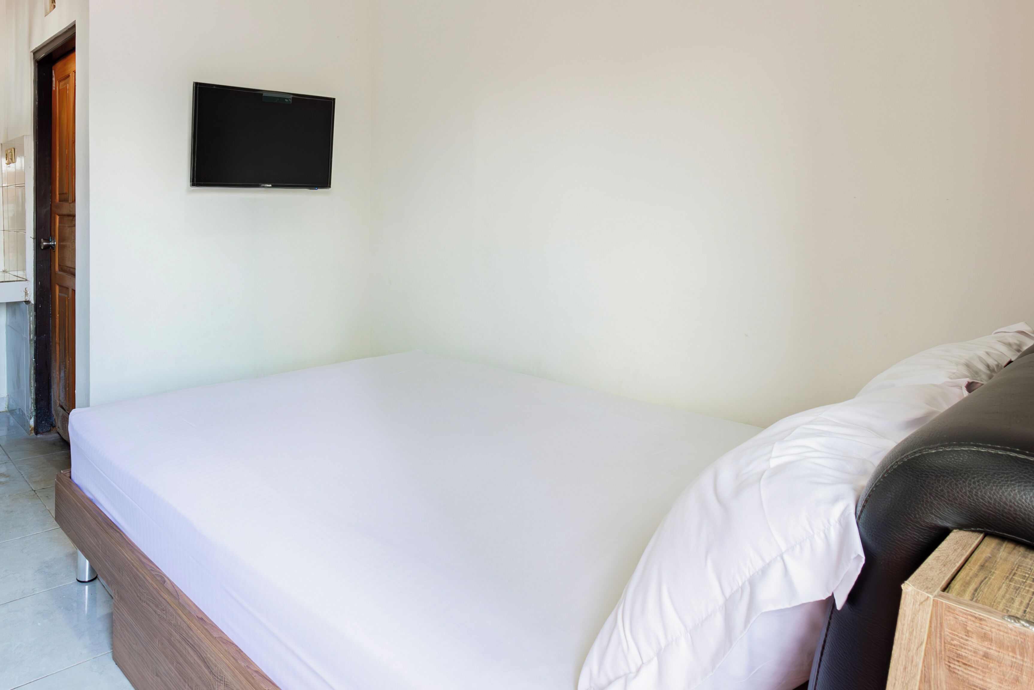 A single bed with a wooden headboard, a white mattress, and a black television mounted on the wall.