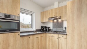 A modern kitchen with wooden cabinets, a built-in oven, a stove, and a coffee maker. - Lakefront Holiday Home (Hoge Hexel)
