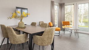 A modern dining area with a table and chairs, a vase of flowers, and a view of trees through large windows. - Lakefront Holiday Home (Hoge Hexel)