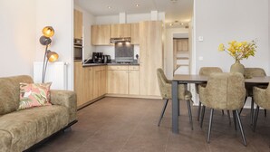 A modern kitchen with wooden cabinets, a dining table with chairs, and a sofa with a floral pillow. - Lakefront Holiday Home (Hoge Hexel)