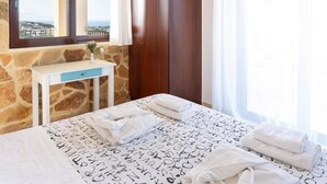 A bedroom with a stone wall, a wooden wardrobe, a bedside table with a vase, and a bed with towels. - Villa Pasiphae 1 in Stalos (Chania)