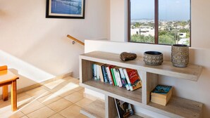 A modern interior with a staircase, a bookshelf with books, decorative vases, and a framed picture of a bridge. - Villa Pasiphae 1 in Stalos (Chania)