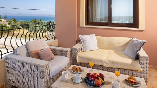 A balcony with wicker furniture, a table with breakfast, and a view of the sea. - Villa Pasiphae 1 in Stalos (Chania)