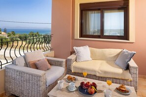A balcony with wicker furniture, a table with breakfast, and a view of the sea. - Villa Pasiphae 1 in Stalos (Chania)