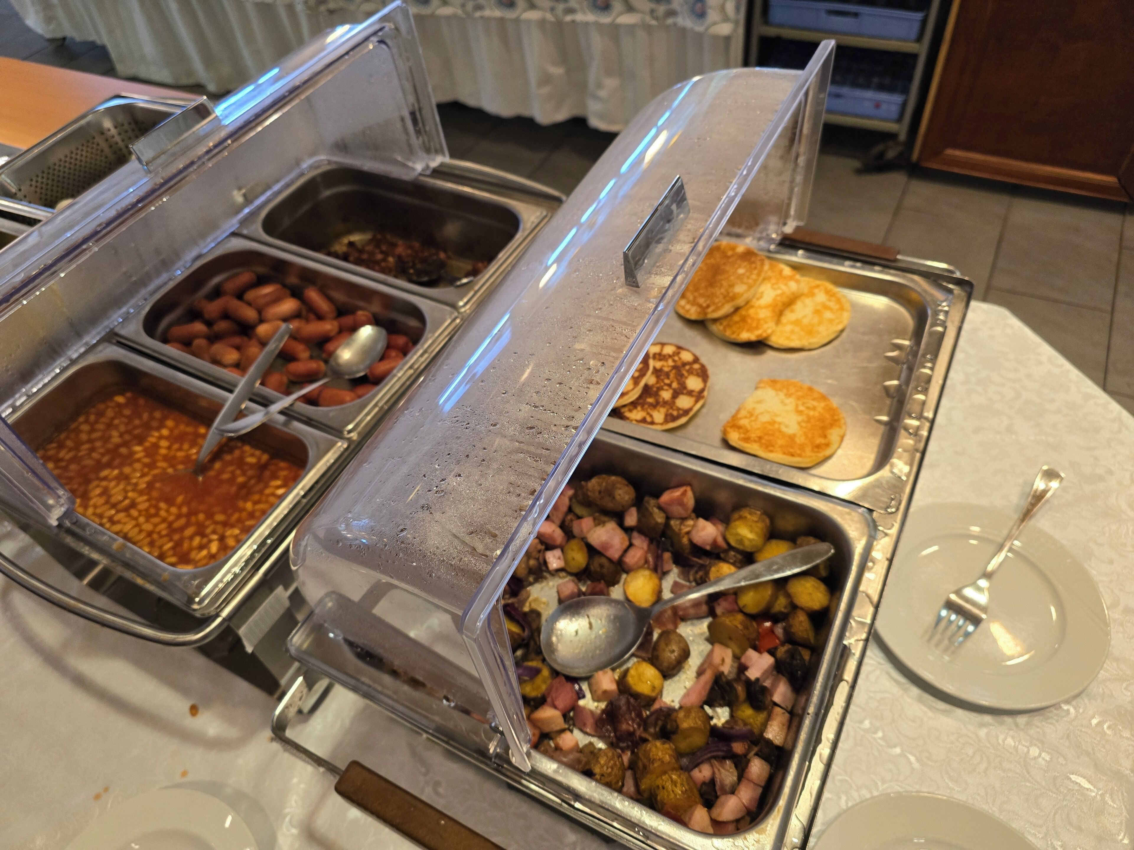 A buffet with various food options including beans, sausages, and pancakes.