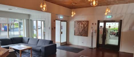 A modern lobby with a sofa, a coffee table, and a patterned rug. There are hanging light fixtures and a door with an exit sign.