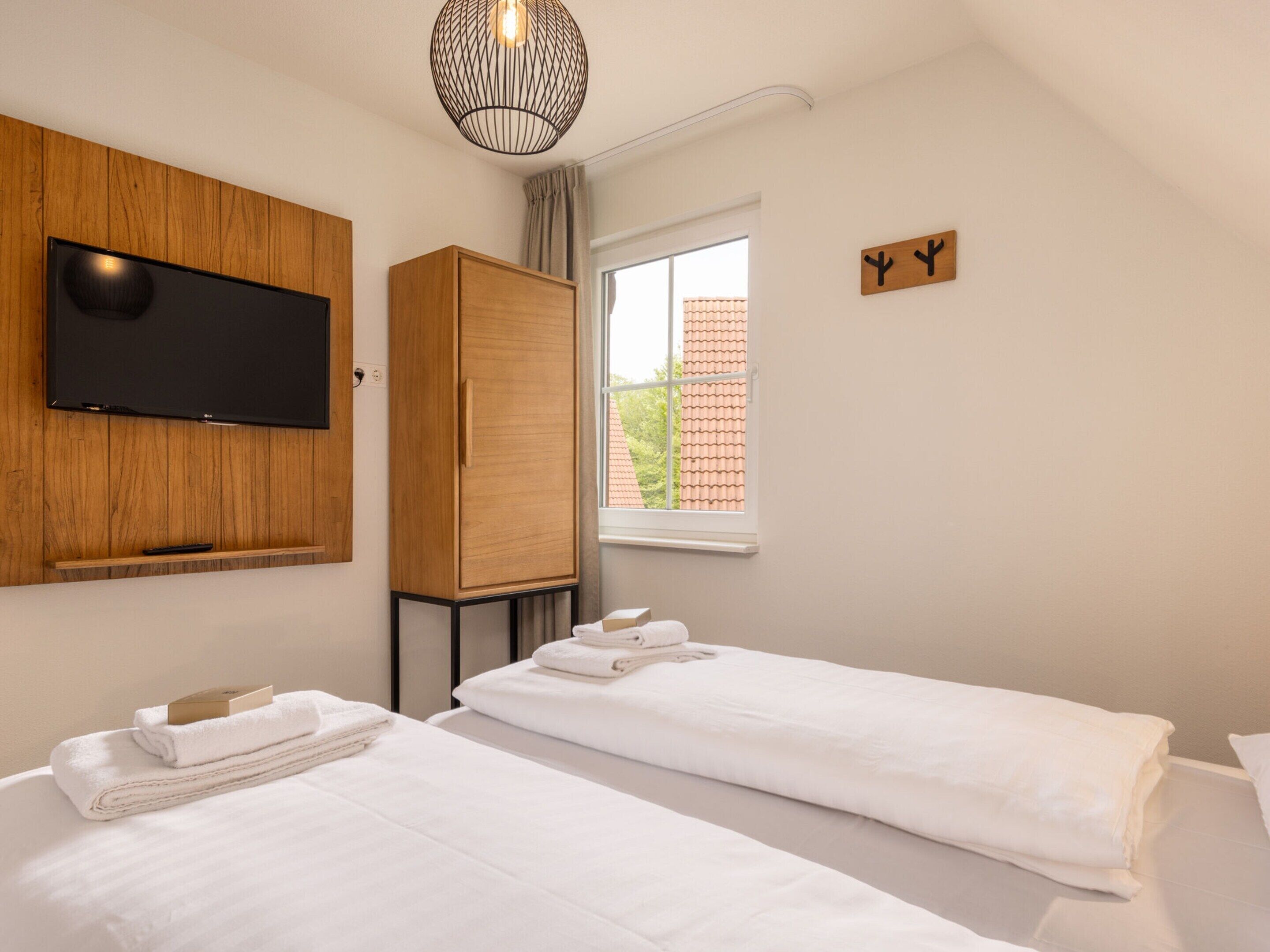 Une chambre d’hôtel moderne avec deux lits, une télévision, une armoire et une fenêtre donnant sur un immeuble.