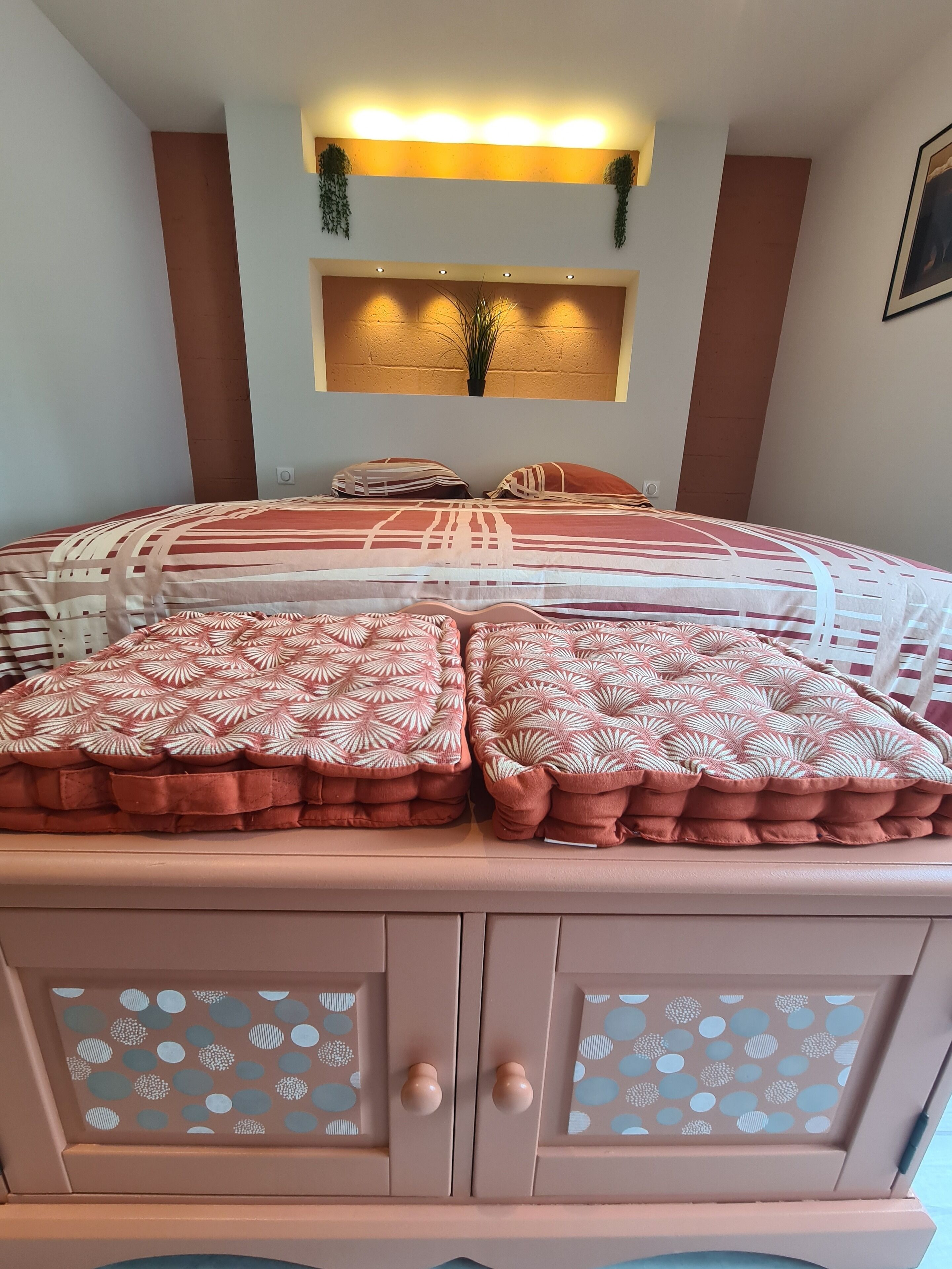 Ein Schlafzimmer mit einem Bett, Kissen, einem Wandregal und einem Schrank mit gemusterten Türen.