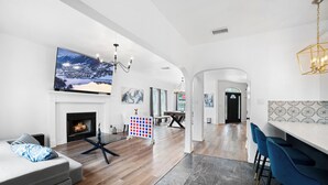 A spacious living room with a fireplace, a large TV, and a modern dining area with bar stools. - Modern 5 BR Sleeps 16 with Pool, Spa, Air Hockey, BBQ & Games Near Downtown! (San Antonio)