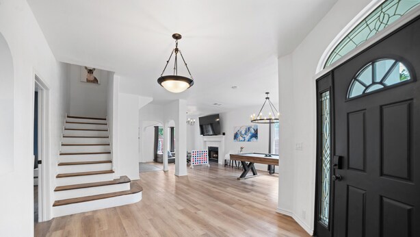 A spacious interior with a wooden staircase, a dining area, and a black door with a glass window. - Modern 5 BR Sleeps 16 with Pool, Spa, Air Hockey, BBQ & Games Near Downtown! (San Antonio)