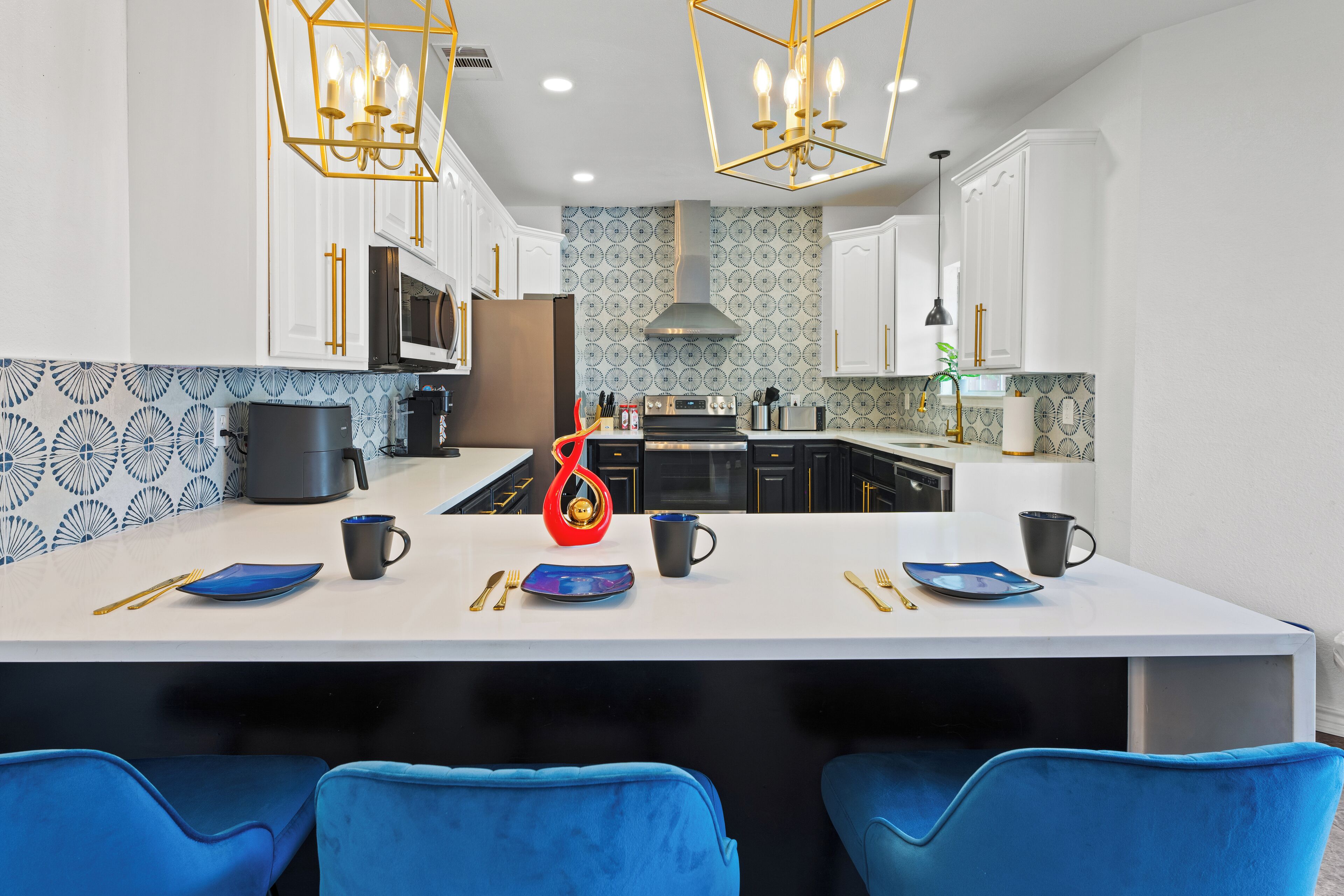 Une cuisine moderne avec des meubles blancs, un îlot central, des chaises bleues et un pare-feu décoratif.
