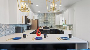 A modern kitchen with white cabinets, a central island, blue chairs, and a patterned backsplash. - Modern 5 BR Sleeps 16 with Pool, Spa, Air Hockey, BBQ & Games Near Downtown! (San Antonio)
