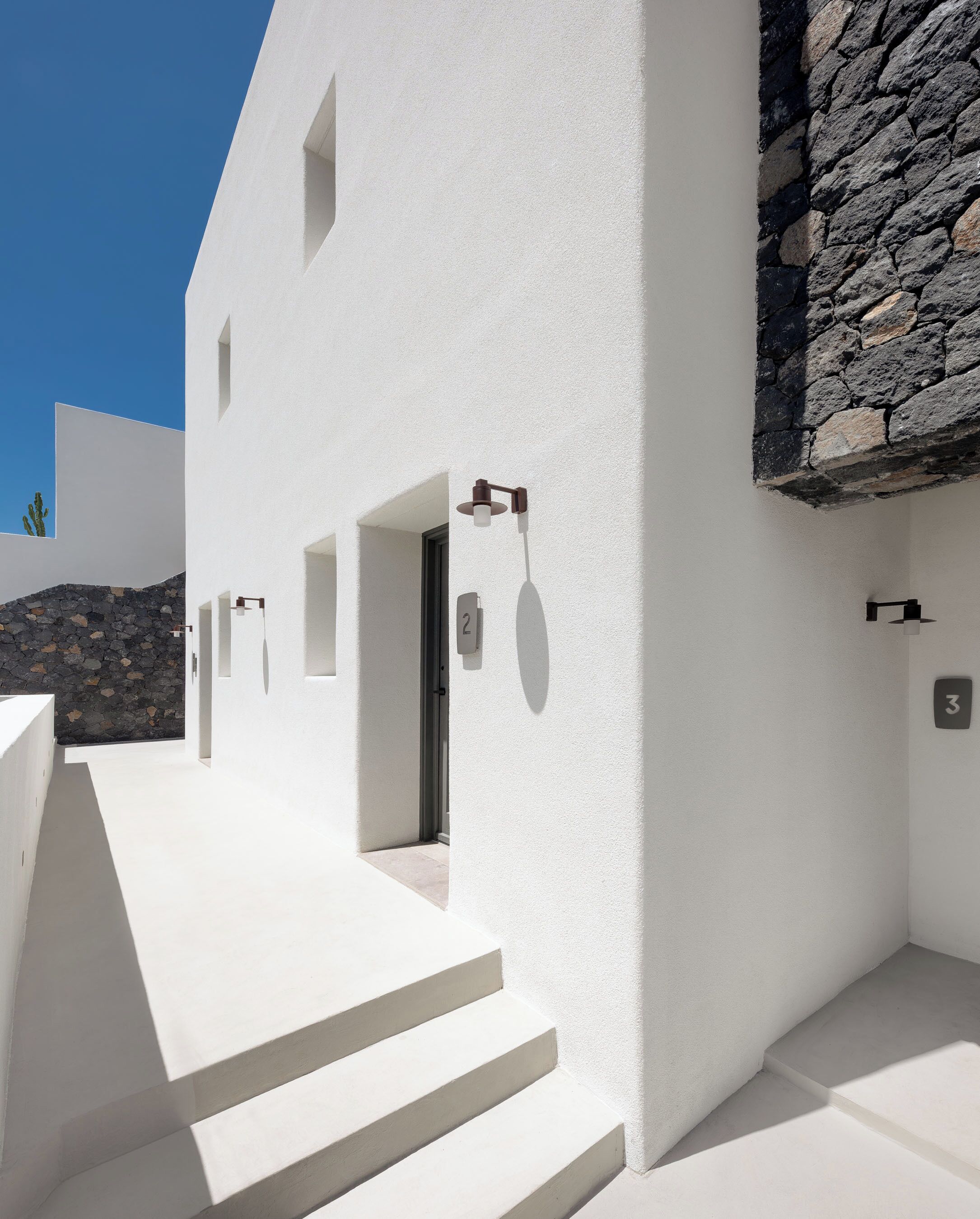 A modern building with white walls, a stone wall, and numbered doors.